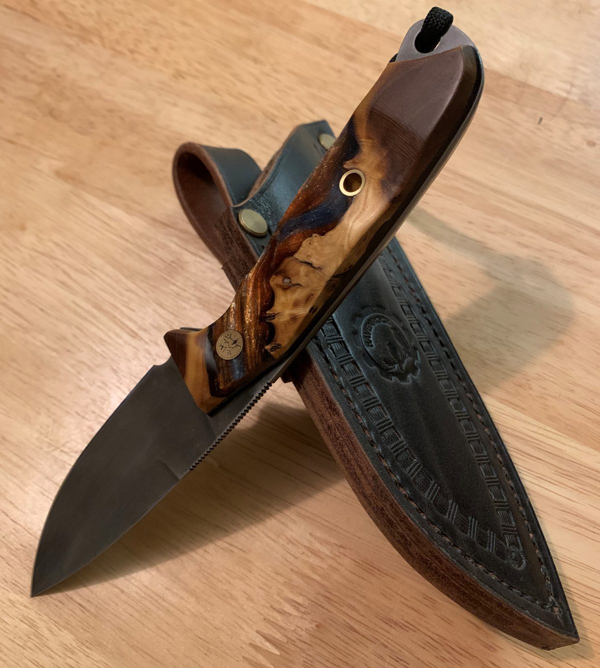 A Ravenrock fixed-blade knife with acid-etched blade and Russian olive burl scales, displayed on its hand-stitched leather sheath.