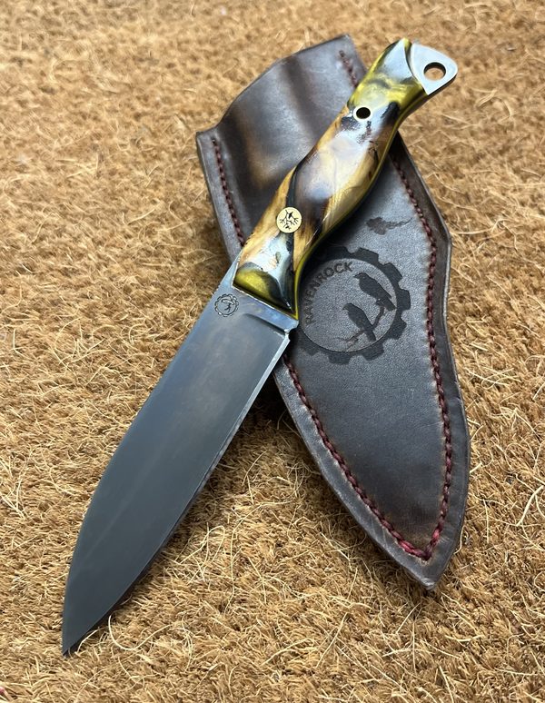 RRK-01-012, upswept blade with deep grey forced patina and swirled olive burl and yellow resin handle, resting on a Ravenrock-stamped leather sheath